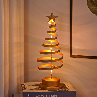 Goldene Spiralbaum-Lampe leuchtet warmweiß auf einem Bücherstapel im abendlichen Wohnzimmer